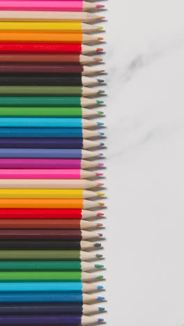 Vertical-Video-Of-Coloured-Pencils-Arranged-In-A-Line-On-White-Marble-Background-